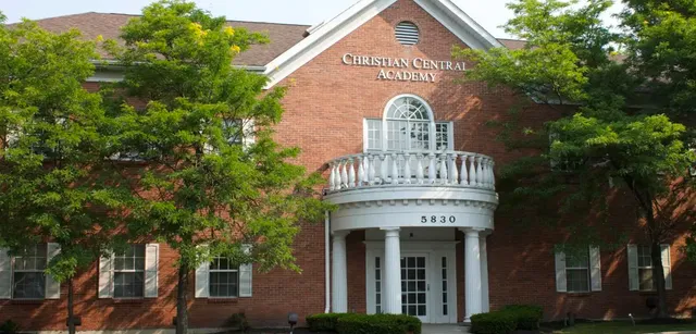 L'edificio in mattoni con un portico bianco e finestre ad arco sul campus della Christian Central Academy è circondato da un fitto verde.