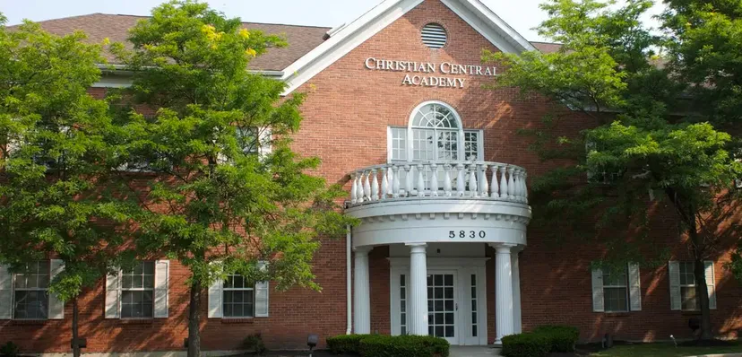 L'edificio in mattoni con un portico bianco e finestre ad arco sul campus della Christian Central Academy è circondato da un fitto verde.