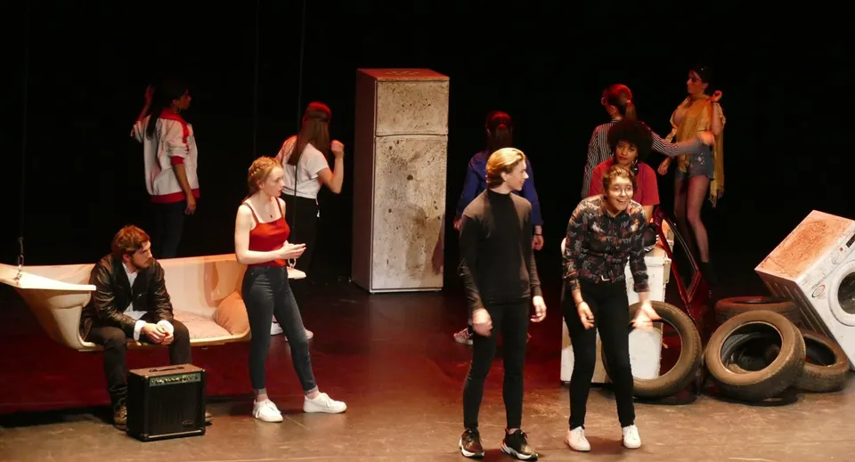 Studenti dell'Institut Saint-Dominique si trovano su un palco con oggetti di scena sullo sfondo.