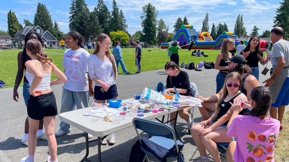 Studenti della Pioneer School Port Coquitlam si riuniscono a un evento nel parco con strutture gonfiabili sullo sfondo.