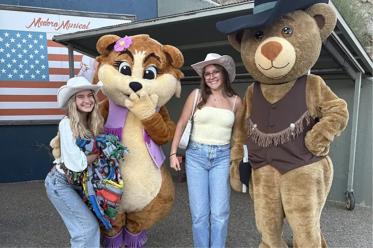 Due studentesse con cappelli da cowboy posano con due mascotte al Medora Musical