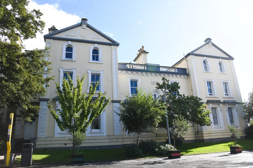 L'edificio bianco a più piani con una complessa architettura nel campus del Plymouth College è circondato da alberi.