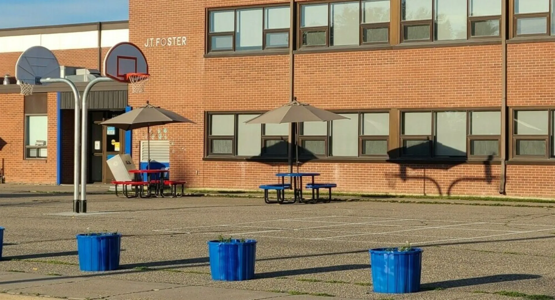 L'edificio in mattoni della J.T. Foster High School con un canestro da basket e diversi bidoni dell'immondizia blu nel piazzale antistante.