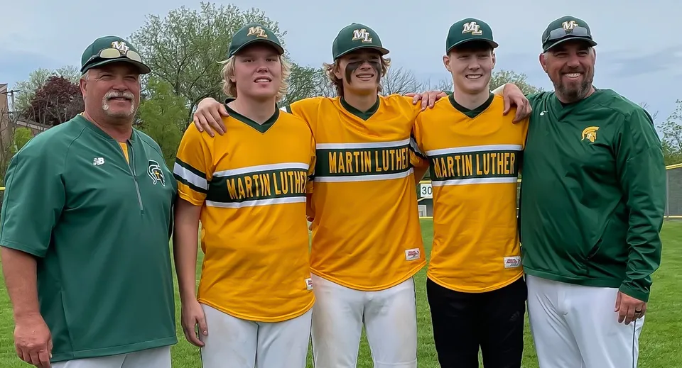Cinque studenti della Martin Luther High School sono insieme all'aperto in divisa da baseball sotto un cielo azzurro.