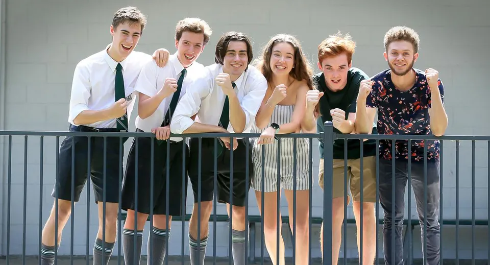 Un gruppo di studenti e studentesse della The Gap State High School sta in piedi davanti a uno sfondo grigio e sorride alla telecamera.