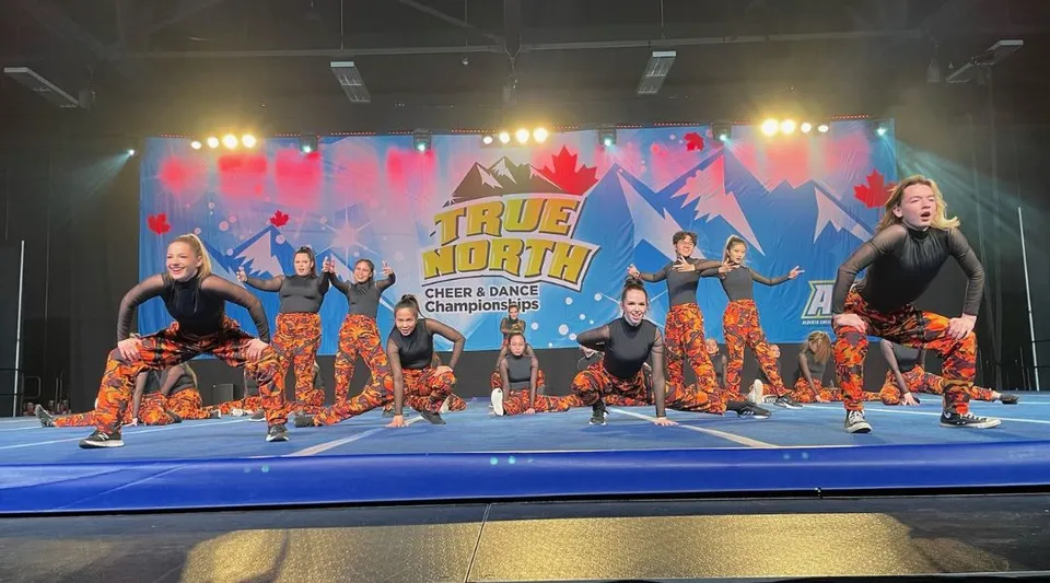 Un gruppo di cheerleader in divise colorate si esibisce sul palco con lo striscione del Tommy Douglas Collegiate.