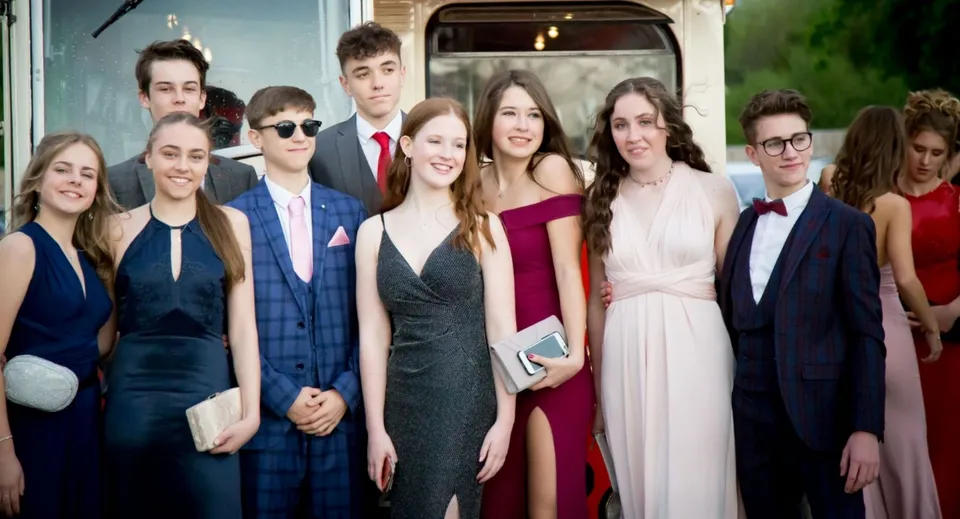 Un gruppo di persone eleganti posa davanti a un edificio durante un evento presso la Our Lady’s Secondary School.
