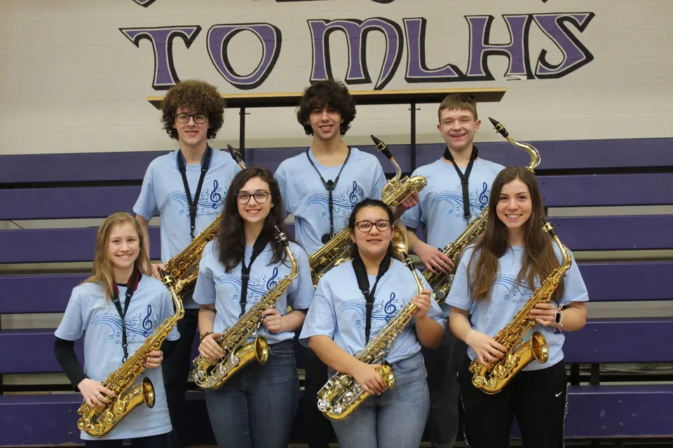 Un gruppo di studenti della Michigan Lutheran High School in uniformi coordinate con saxofoni davanti alla grande insegna Tomcats.