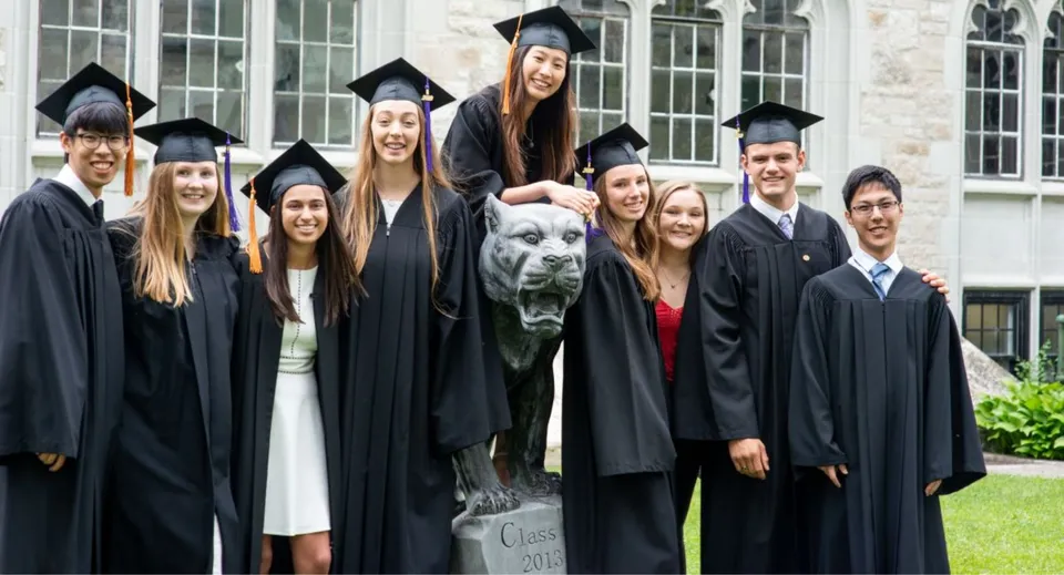 Un gruppo di diplomati e diplomate e un cane posano davanti a un edificio del campus dell'Albert College.