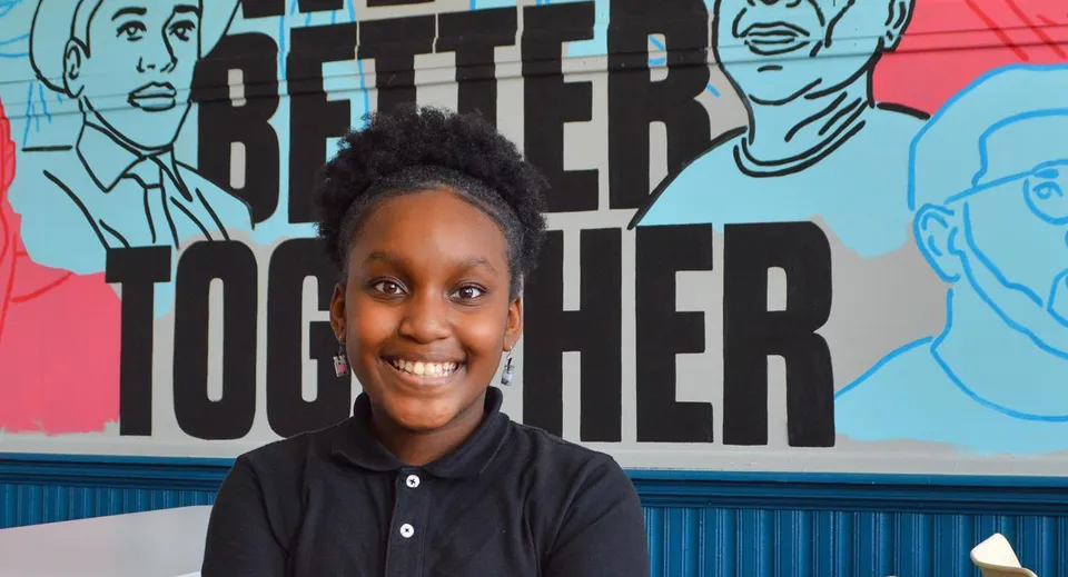 Un ragazzo sta davanti a un murale colorato con la scritta 'Better Together' sul terreno delle Chicago Public Schools.