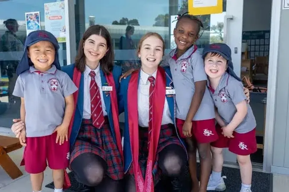 Cinque studenti di diverse età della John Septimus Roe Anglican Community School sorridono in divisa scolastica davanti a un edificio.
