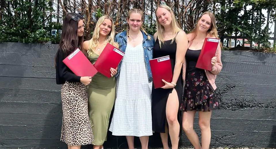 Un gruppo di giovani studentesse si trova davanti a una staccionata di legno nel verde all'interno del campus della Te Puke High School.