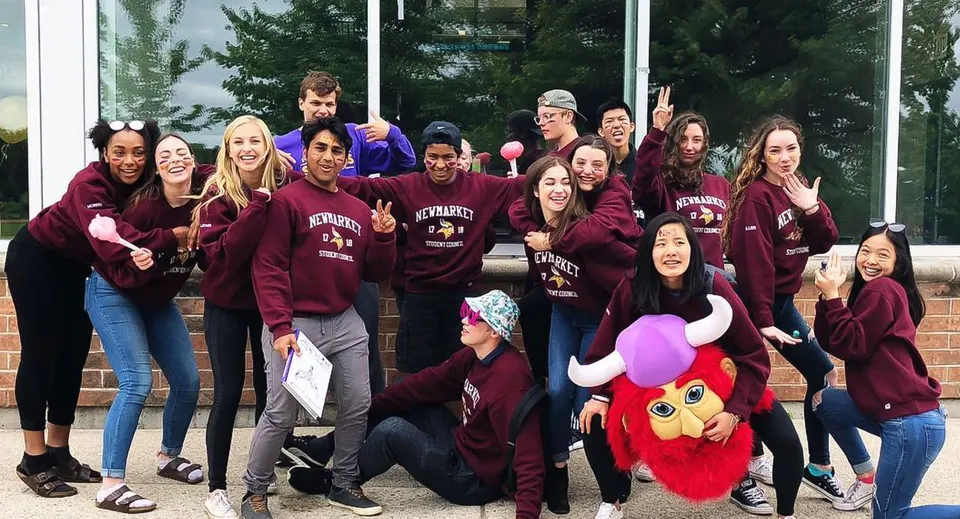 Un gruppo di studenti della Newmarket High School davanti a un edificio con grandi finestre e alberi.