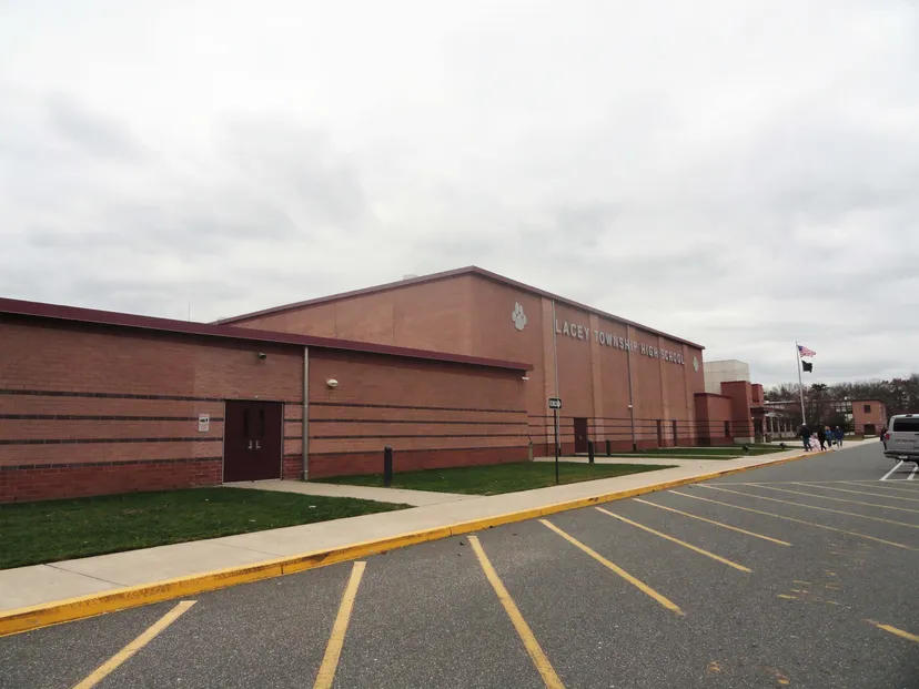 Il grande edificio in mattoni con tetto rosso della Lacey Township High School è circondato da un parcheggio e da spazi verdi.