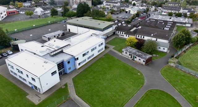 Il vasto campus della Scoil Dara con architettura moderna e tradizionale in mezzo a prati verdi e alberi in una città pittoresca.