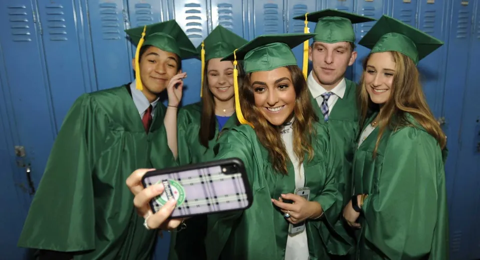 Un gruppo di diplomati della Mitchell District High School in toga verde posa davanti ad armadietti scolastici blu.
