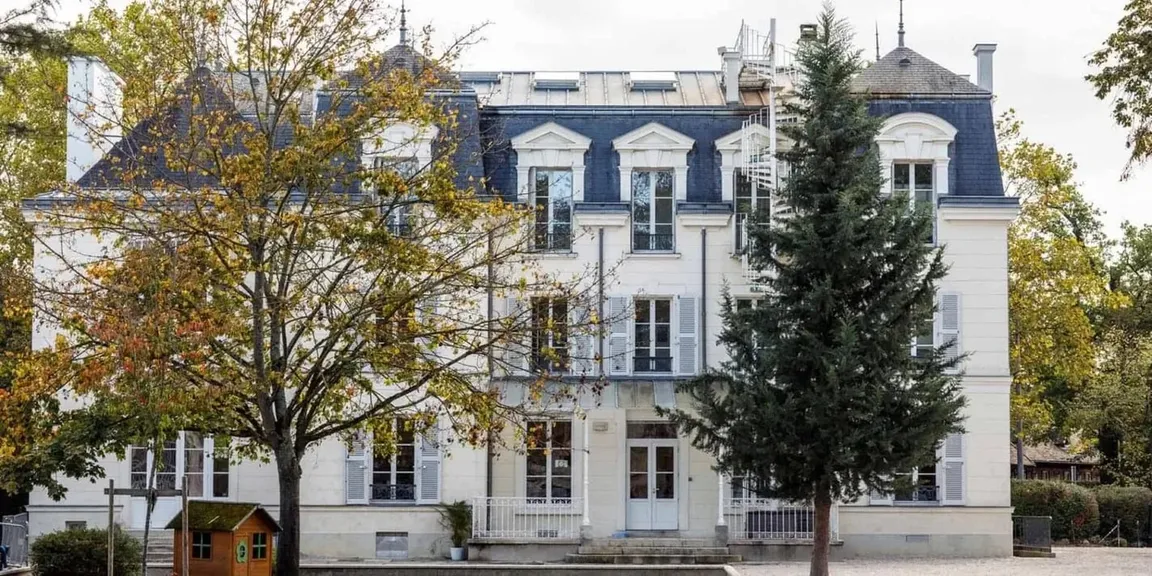 Herrschaftliches Internatsgebäude mit Mansarddach, Fensterläden und Bäumen im Herbstlaub davor