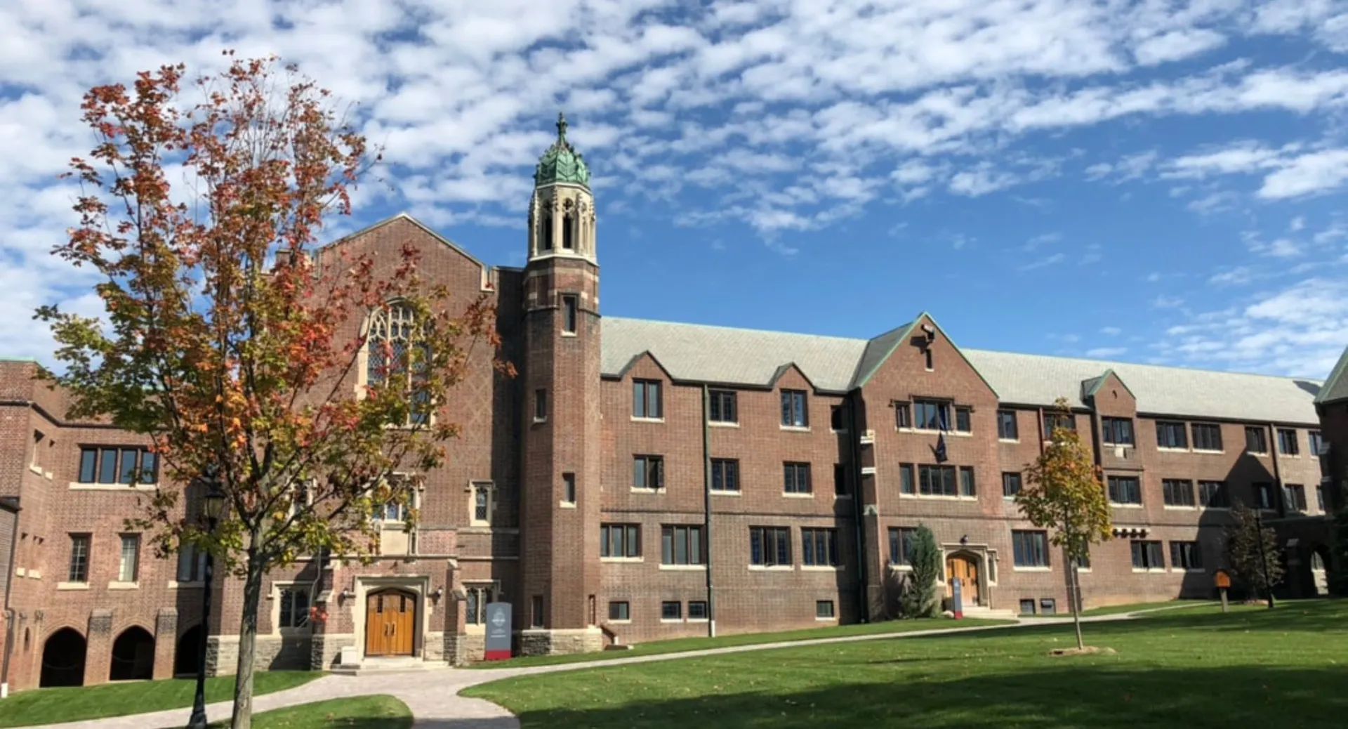 L'edificio in mattoni a più piani con un'alta torre nel campus della Trinity College School è circondato da alberi e prati.