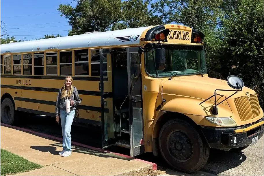 Estudiante con una botella en la mano junto a un autobús escolar amarillo estadounidense