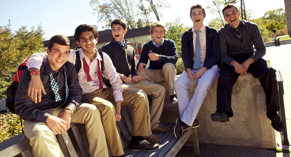 Un gruppo di giovani uomini in abito formale siede su un muretto di pietra nel campus della The Hun School of Princeton.