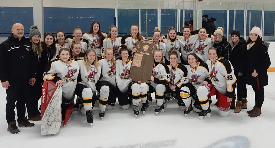 Un gruppo di giovani giocatrici di hockey della Centre Wellington District High School si trova sul ghiaccio e festeggia con un trofeo.