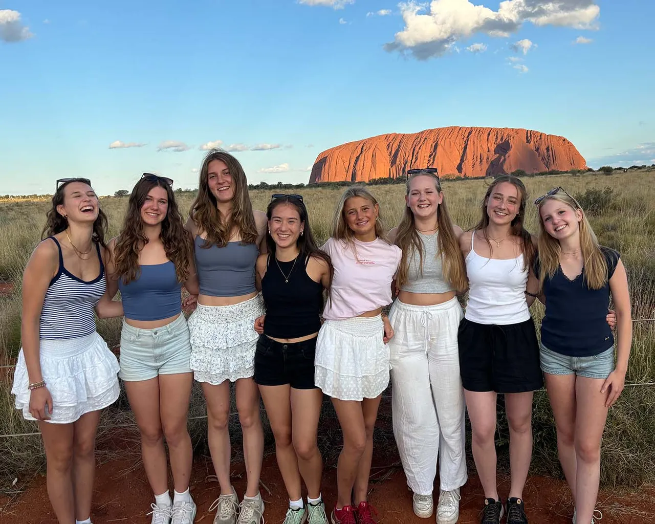 Ocho chicas abrazadas ante la roca de Uluru al atardecer, en el interior de Australia