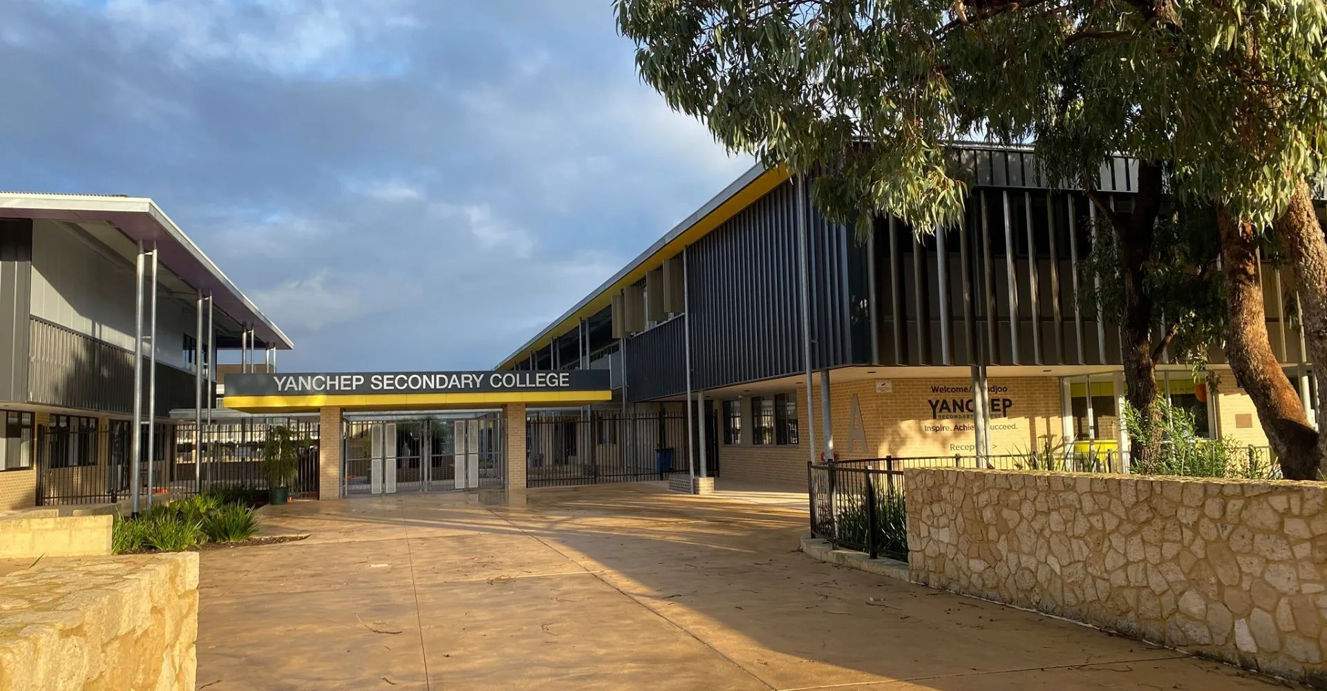 L'edificio scolastico moderno a più piani del Yanchep Secondary College è circondato da alberi e da un viale pavimentato.
