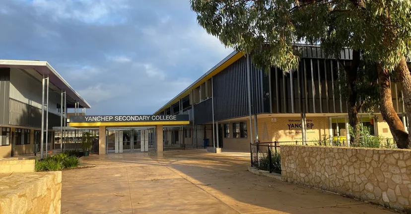 L'edificio scolastico moderno a più piani del Yanchep Secondary College è circondato da alberi e da un viale pavimentato.