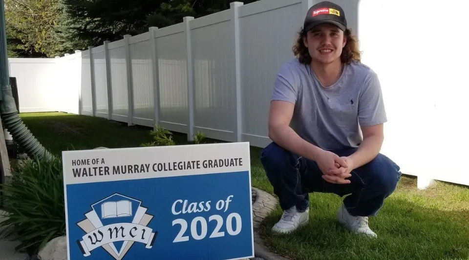 Uno studente siede accanto a un cartello della Walter Murray Collegiate Graduate Class of 2020.