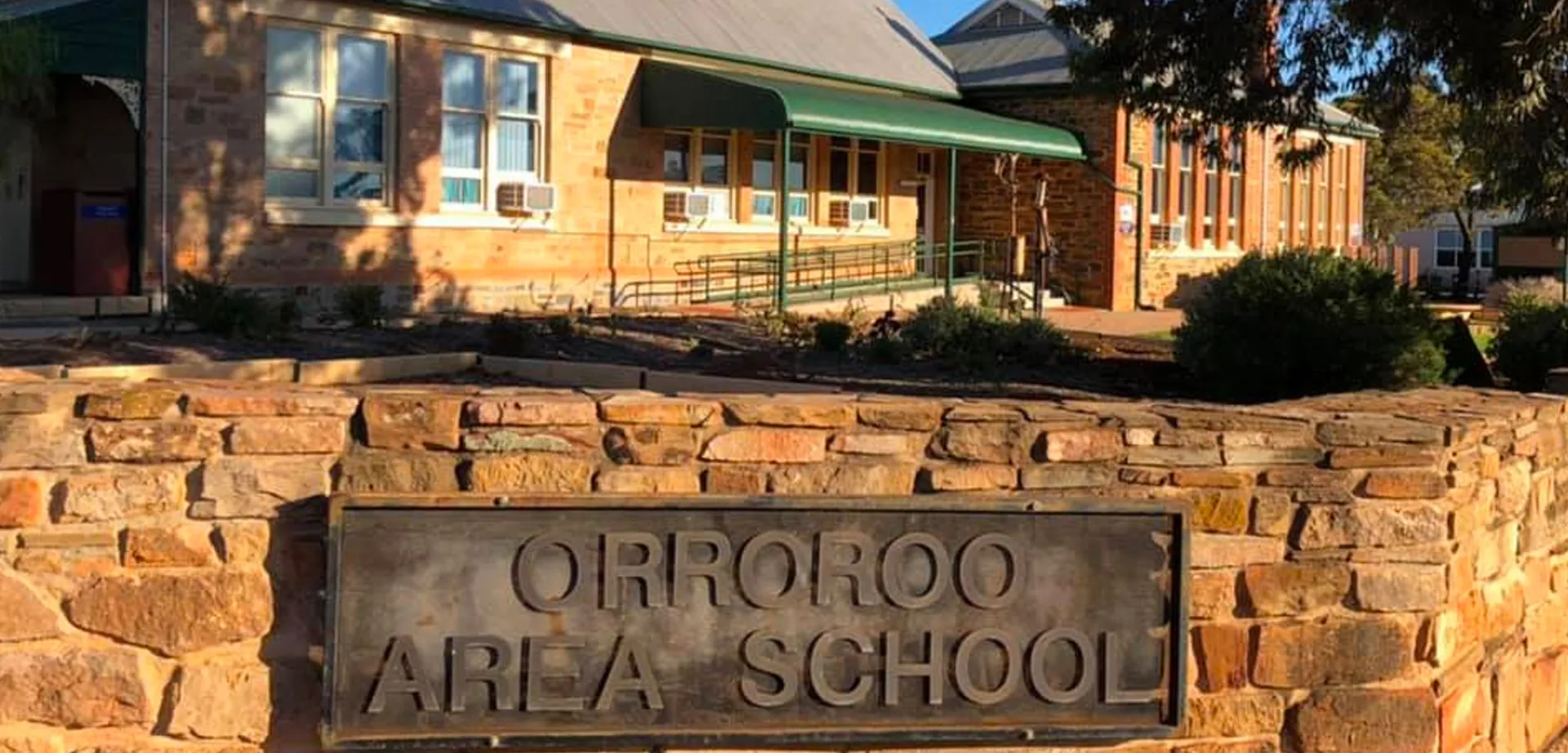 Il cartello d'ingresso della Orroroo Area School si trova davanti a un edificio in mattoni con alberi sullo sfondo.