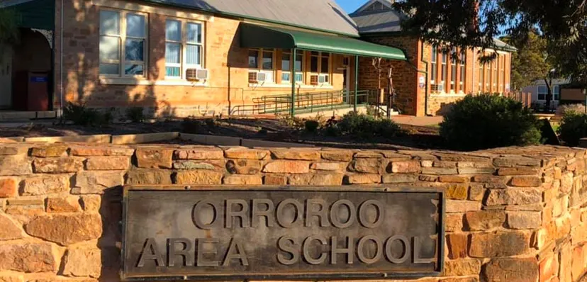 Il cartello d'ingresso della Orroroo Area School si trova davanti a un edificio in mattoni con alberi sullo sfondo.