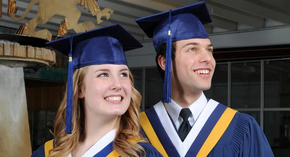Due diplomati in toga blu si trovano nell'edificio scolastico della Laurier MacDonald High School.
