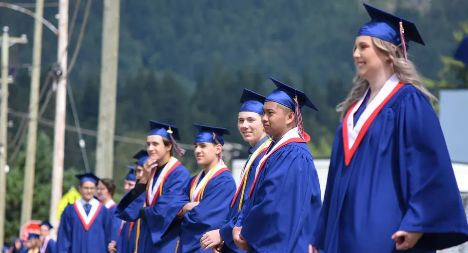 Un gruppo di diplomati della Norwell District Secondary School posa insieme con la toga blu da diploma davanti a uno sfondo alberato.