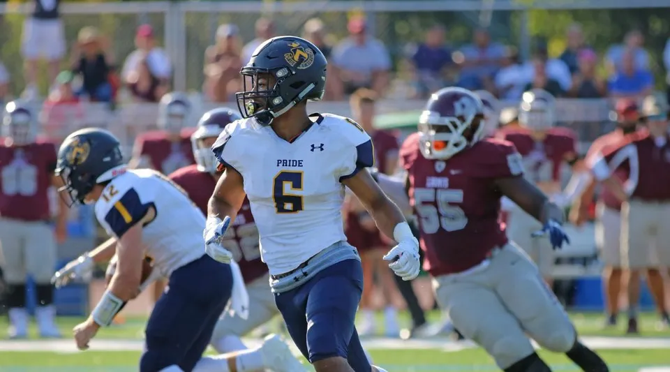Un giocatore di football della Trinity-Pawling School è in piedi sul campo accanto ad altri giocatori con maglie diverse.