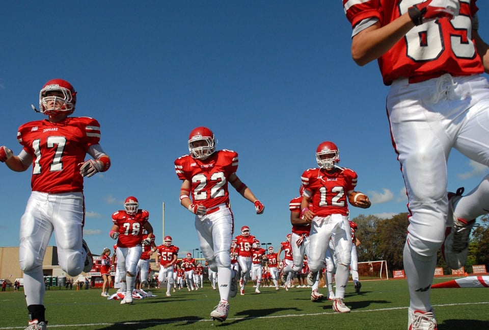 Giocatori di football americano di Neufundland und Labrador corrono sul campo con divise rosse e bianche.