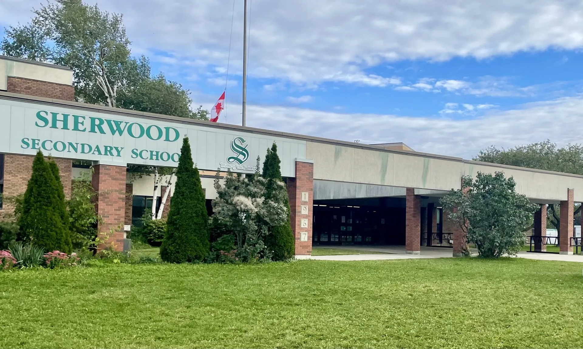 Entrada de la Sherwood Secondary School en Hamilton con el rótulo verde, pilares de ladrillo y césped delante