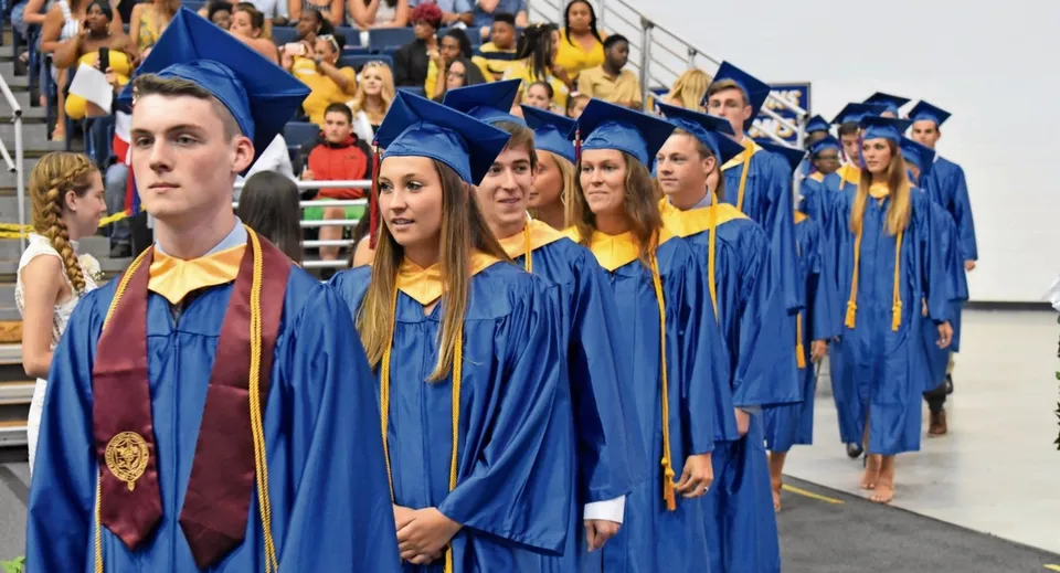 Diplomate e diplomati della Northwest Christian High School in toga e tocco blu e gialli mentre camminano insieme.