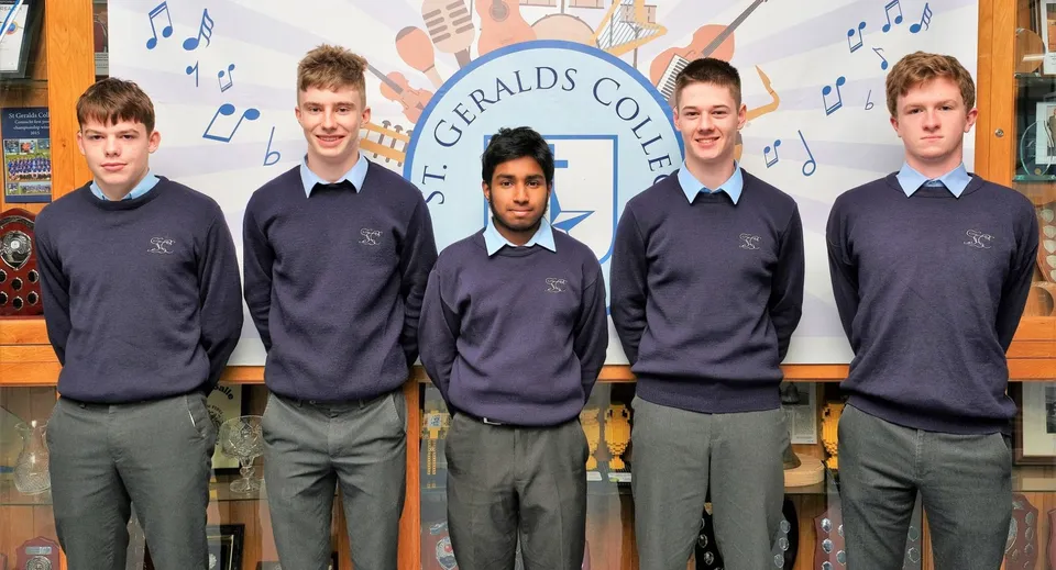 Cinque studenti in divisa scolastica sono in piedi davanti a uno sfondo con il nome St. Gerald's College e note musicali.