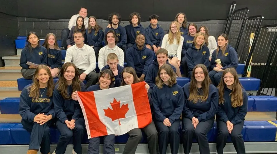 Un gruppo di studentesse in divisa della St. Anne Catholic High School tiene insieme una bandiera canadese.