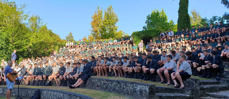Un gruppo di studenti seduto su un muretto in pietra sotto gli alberi nel campus del Rathkeale College con cielo terso.
