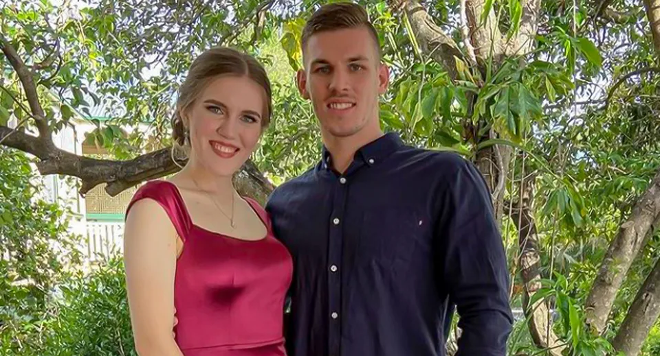 Una giovane coppia sorridente si trova all'aperto nel verde del campus della Mount Gravatt State High School.