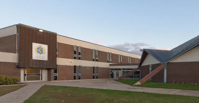 L'edificio in mattoni a più piani con il logo dell'Evan Hardy Collegiate sorge su un terreno verde sotto un cielo blu.