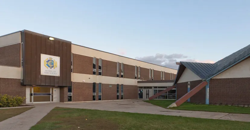 L'edificio in mattoni a più piani con il logo dell'Evan Hardy Collegiate sorge su un terreno verde sotto un cielo blu.
