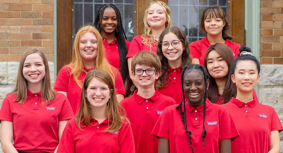 Un gruppo di studentesse della Dominion Academy of Dayton posa sorridente davanti a un edificio in mattoni.
