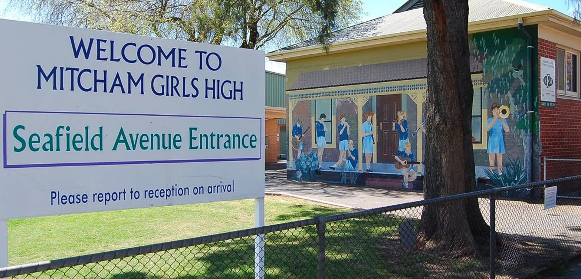 L'ingresso della Mitcham Girls High School con un cartello di benvenuto, un murale e una recinzione davanti a un prato.