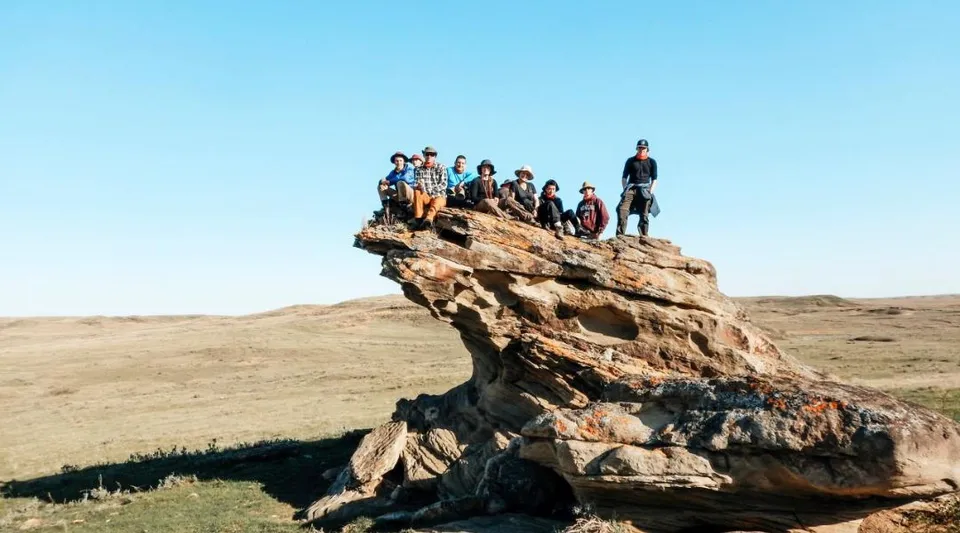 Un gruppo di studenti della Marion M. Graham Collegiate è seduto e in piedi su una grande formazione rocciosa in un paesaggio aperto.