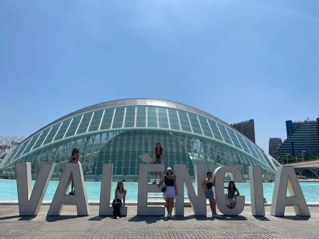 Gruppo di ragazze in posa davanti alle grandi lettere "Valencia" con architettura moderna sullo sfondo