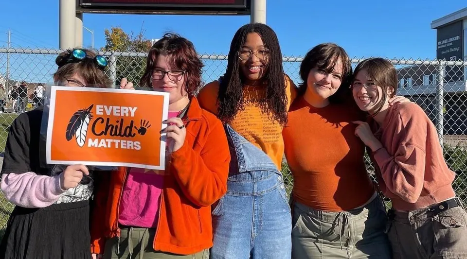 Un gruppo di giovani ragazze con un cartello 'Every Child Matters' si trova davanti a una recinzione nell'area della Maxwell Heights Secondary School.
