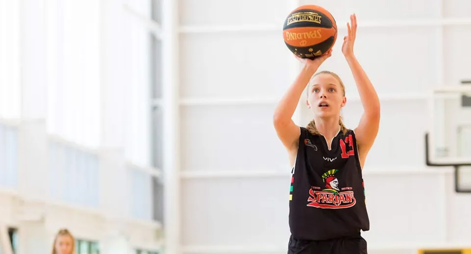 Una giovane giocatrice di basket della Wellington Point State High School salta in palestra e raggiunge la palla.