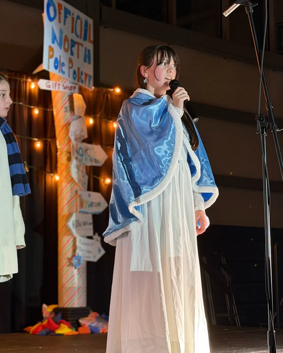 Una studentessa della Aspengrove School in costume con un mantello blu parla al microfono su un palco.